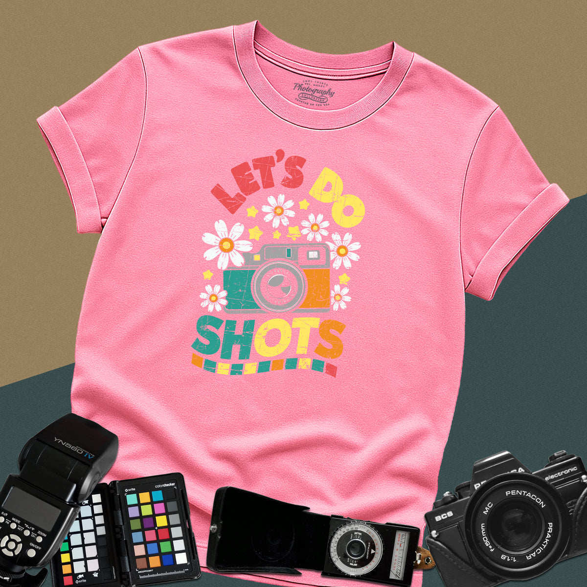 An azalea t-shirt featuring a colorful distressed retro graphic with a camera, daisies, and stars between the text "LET'S DO" and "SHOTS" in bold block letters.