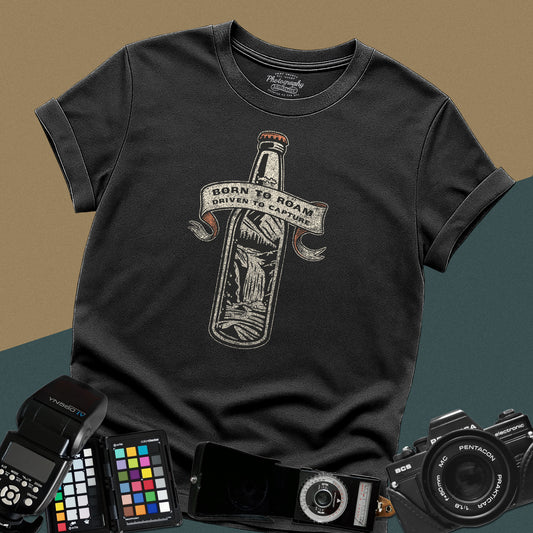 Vintage black graphic t-shirt featuring a bottle with a mountain landscape and the text "Born to Roam Driven to Capture" for travel photographers.