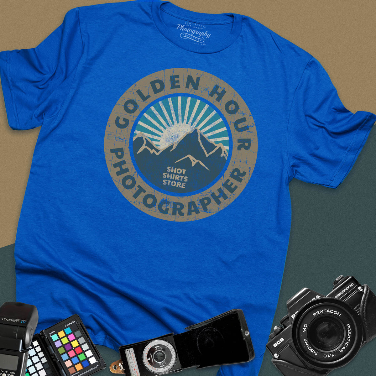 A royal blue t-shirt featuring a distressed circular vintage badge design with mountain peaks and sunburst rays, surrounded by the text "Golden Hour Photographer" written along the border.