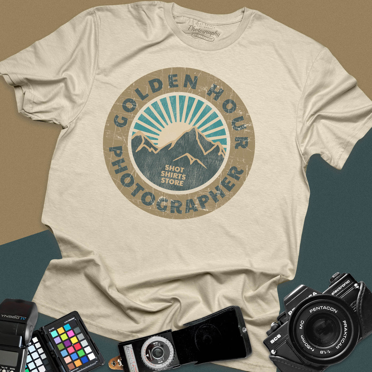 A sand t-shirt featuring a distressed circular vintage badge design with mountain peaks and sunburst rays, surrounded by the text "Golden Hour Photographer" written along the border.