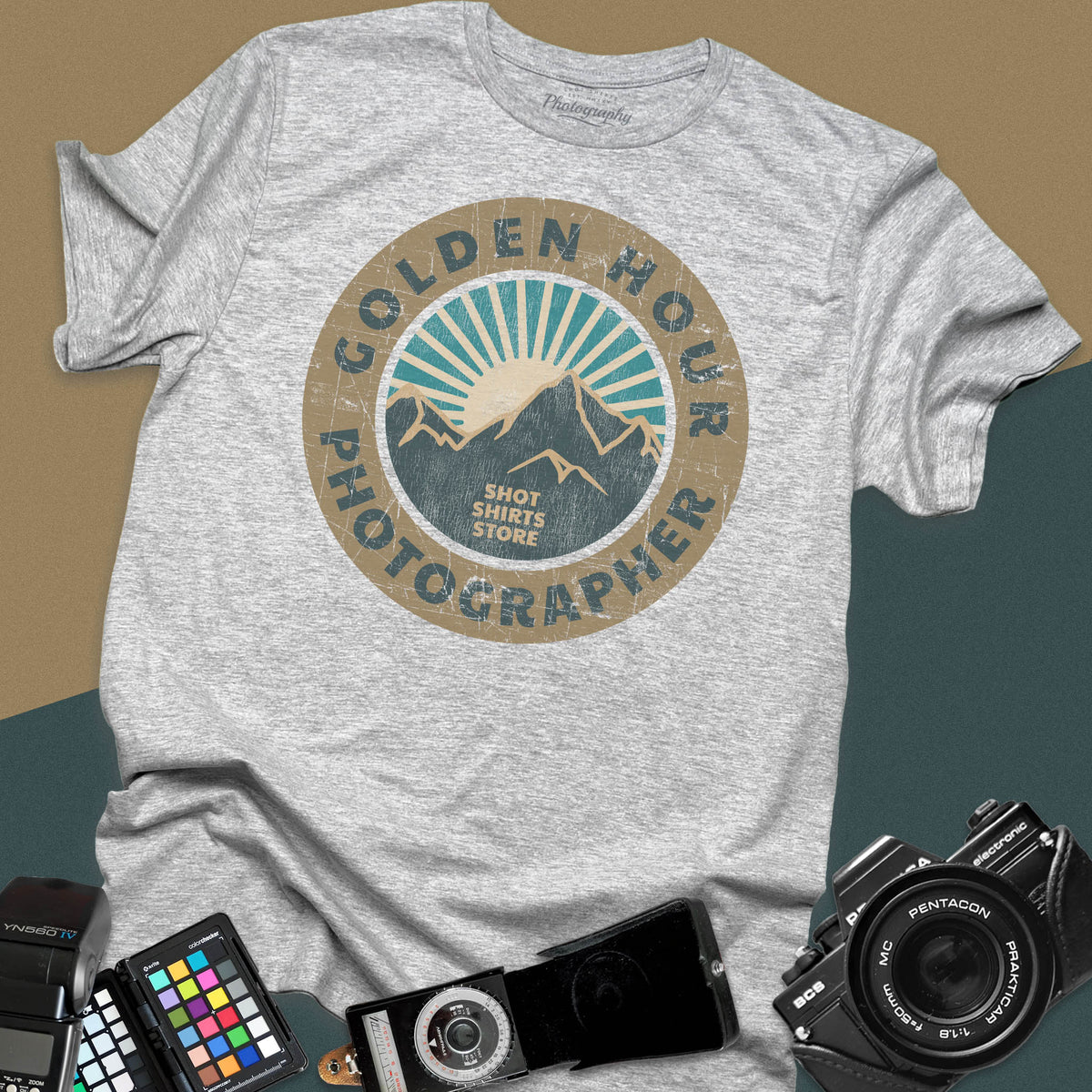 A sport grey t-shirt featuring a distressed circular vintage badge design with mountain peaks and sunburst rays, surrounded by the text "Golden Hour Photographer" written along the border.