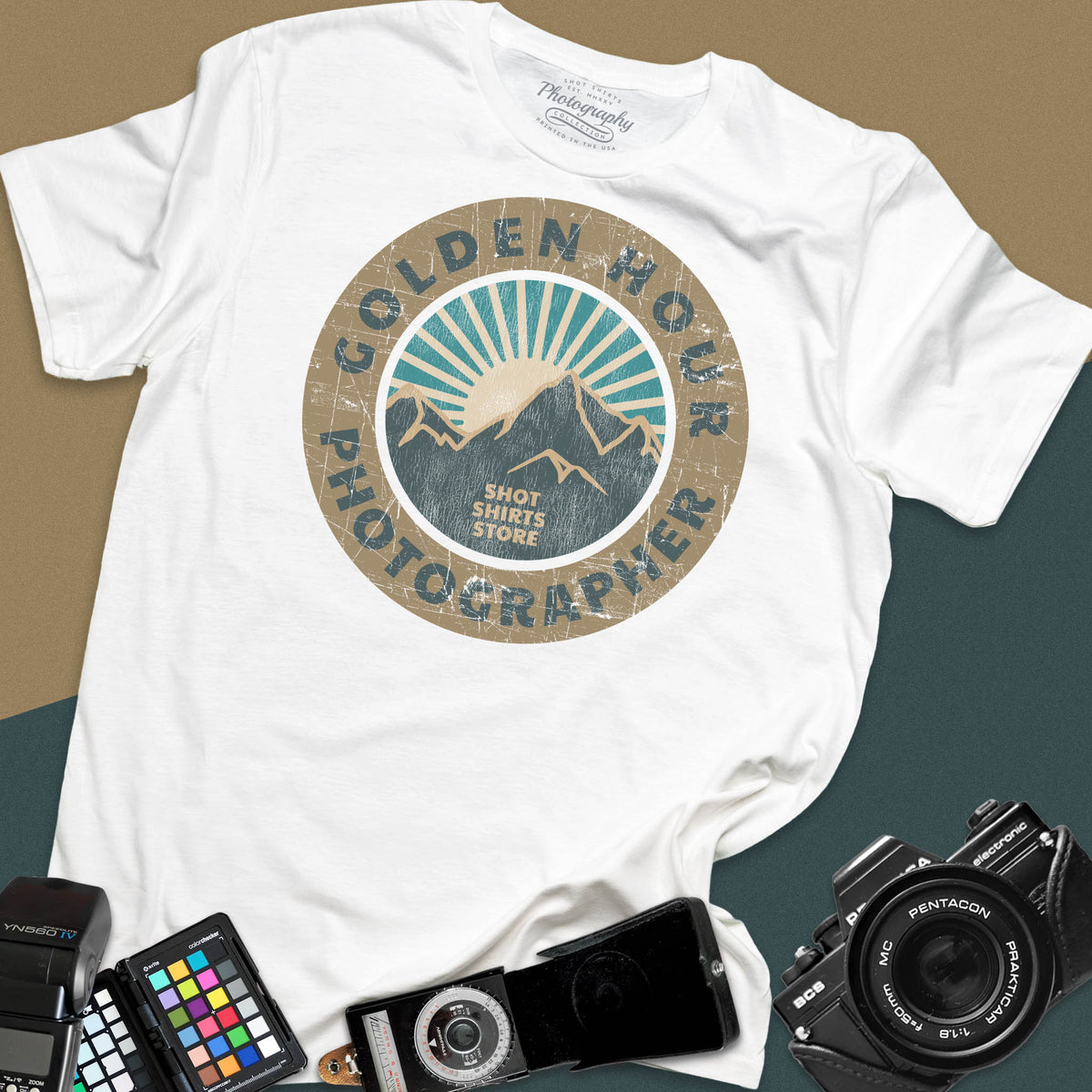 A white t-shirt featuring a distressed circular vintage badge design with mountain peaks and sunburst rays, surrounded by the text "Golden Hour Photographer" written along the border.
