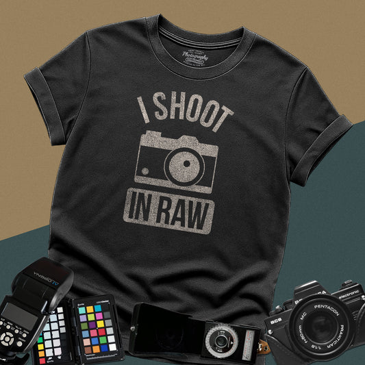 Heavy distressed black t-shirt featuring a retro rangefinder camera illustration with bold arched typography text I Shoot In Raw for professional visual creators.