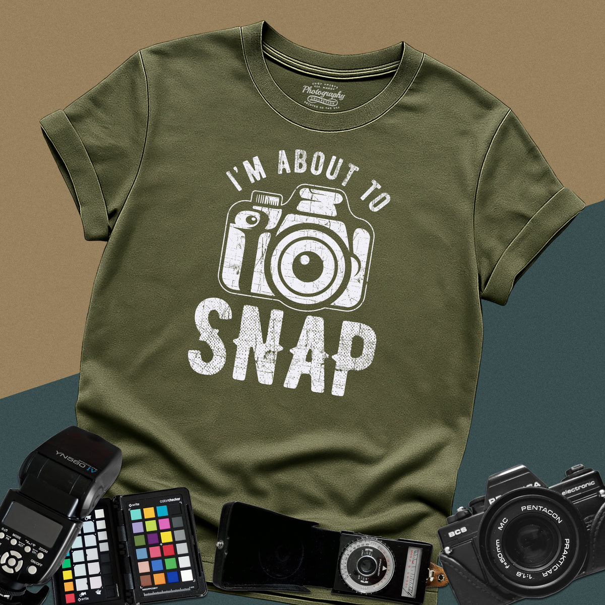 A military-green t-shirt featuring a distressed modern camera graphic centered between the text "I'm about to" in a curved font above and "SNAP" written in large block letters below.