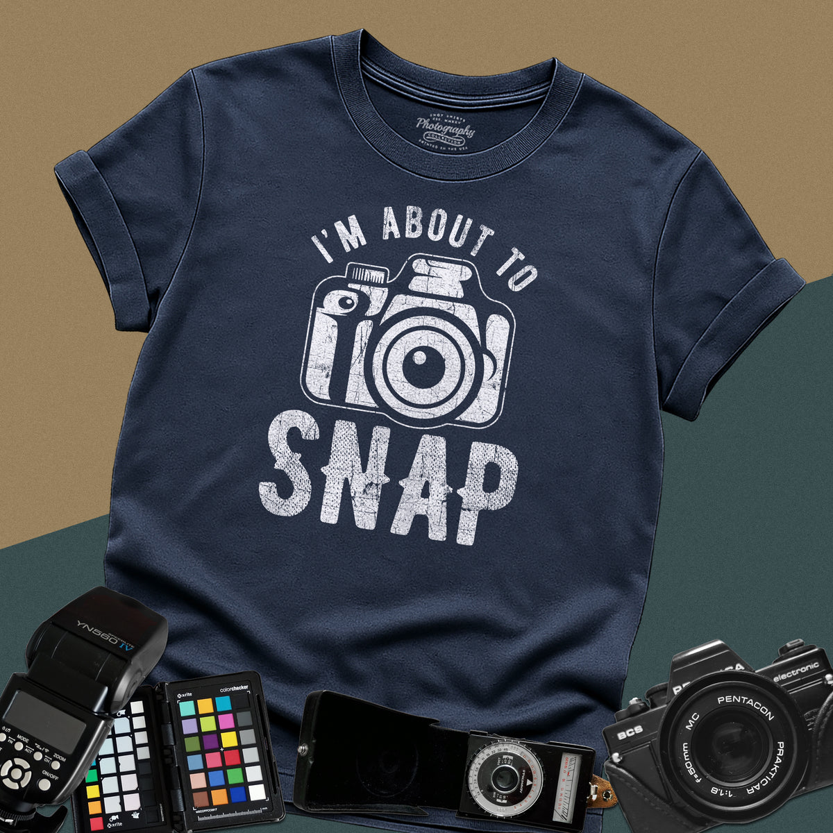 A navy-blue t-shirt featuring a distressed modern camera graphic centered between the text "I'm about to" in a curved font above and "SNAP" written in large block letters below.