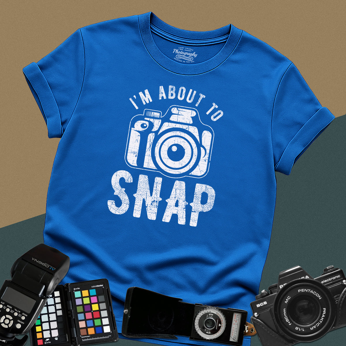 A royal-blue t-shirt featuring a distressed modern camera graphic centered between the text "I'm about to" in a curved font above and "SNAP" written in large block letters below.