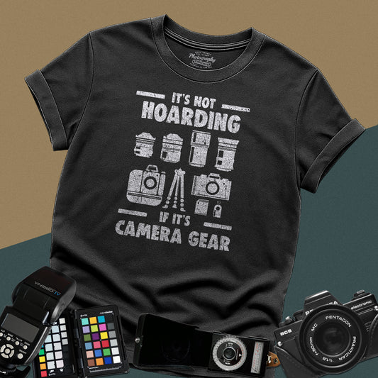 A black t-shirt featuring a distressed graphic with illustrations of camera bodies, lenses, and a tripod between the text "IT'S NOT HOARDING" and "IF IT'S CAMERA GEAR."