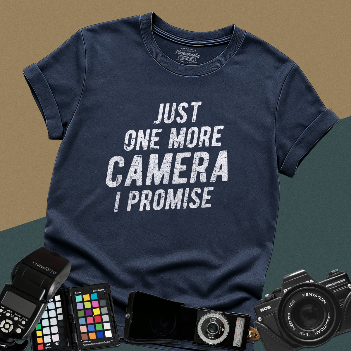 A navy-blue t-shirt featuring a distressed typography design that reads "JUST ONE MORE CAMERA I PROMISE" in bold letters across the chest.