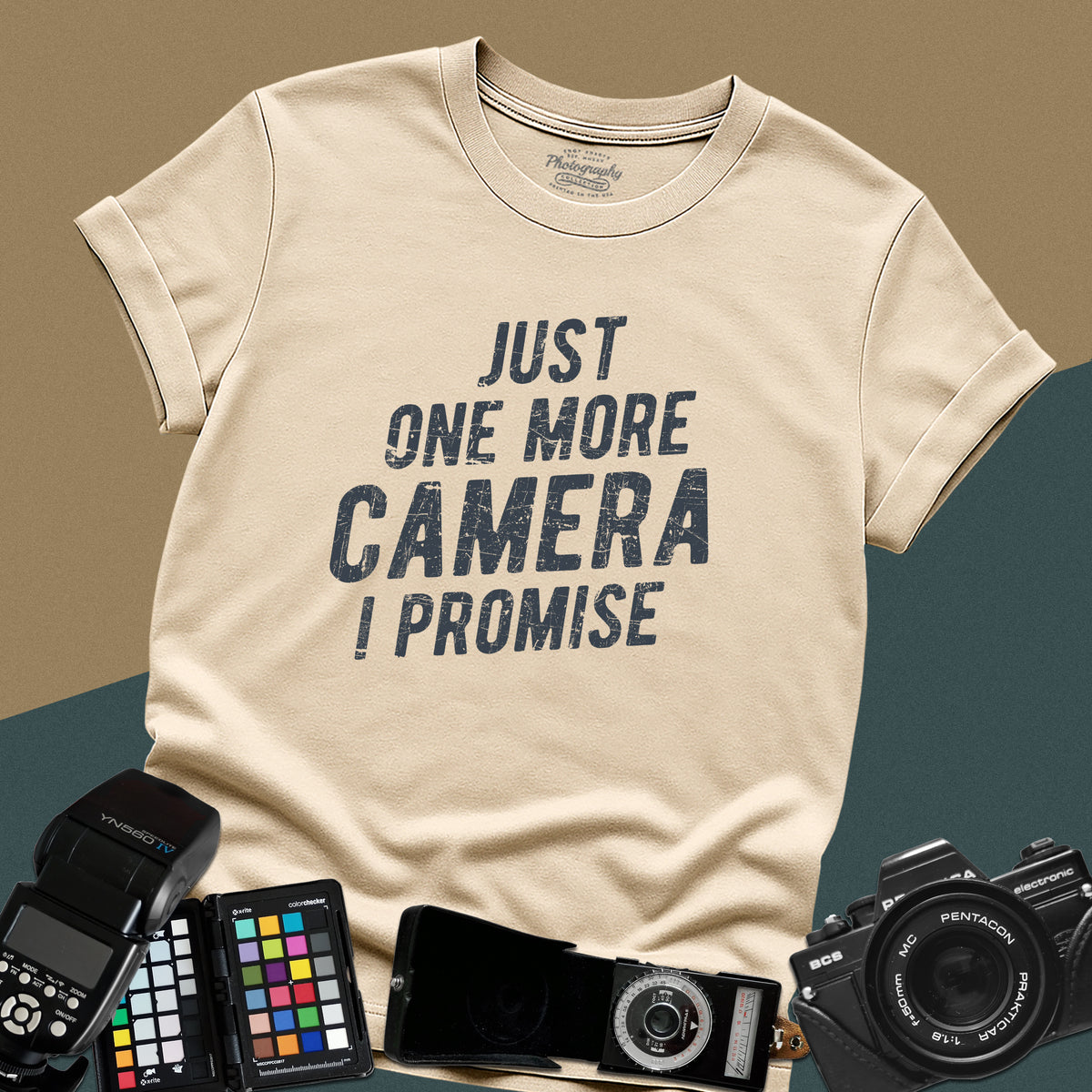 A sand t-shirt featuring a distressed typography design that reads "JUST ONE MORE CAMERA I PROMISE" in bold letters across the chest.
