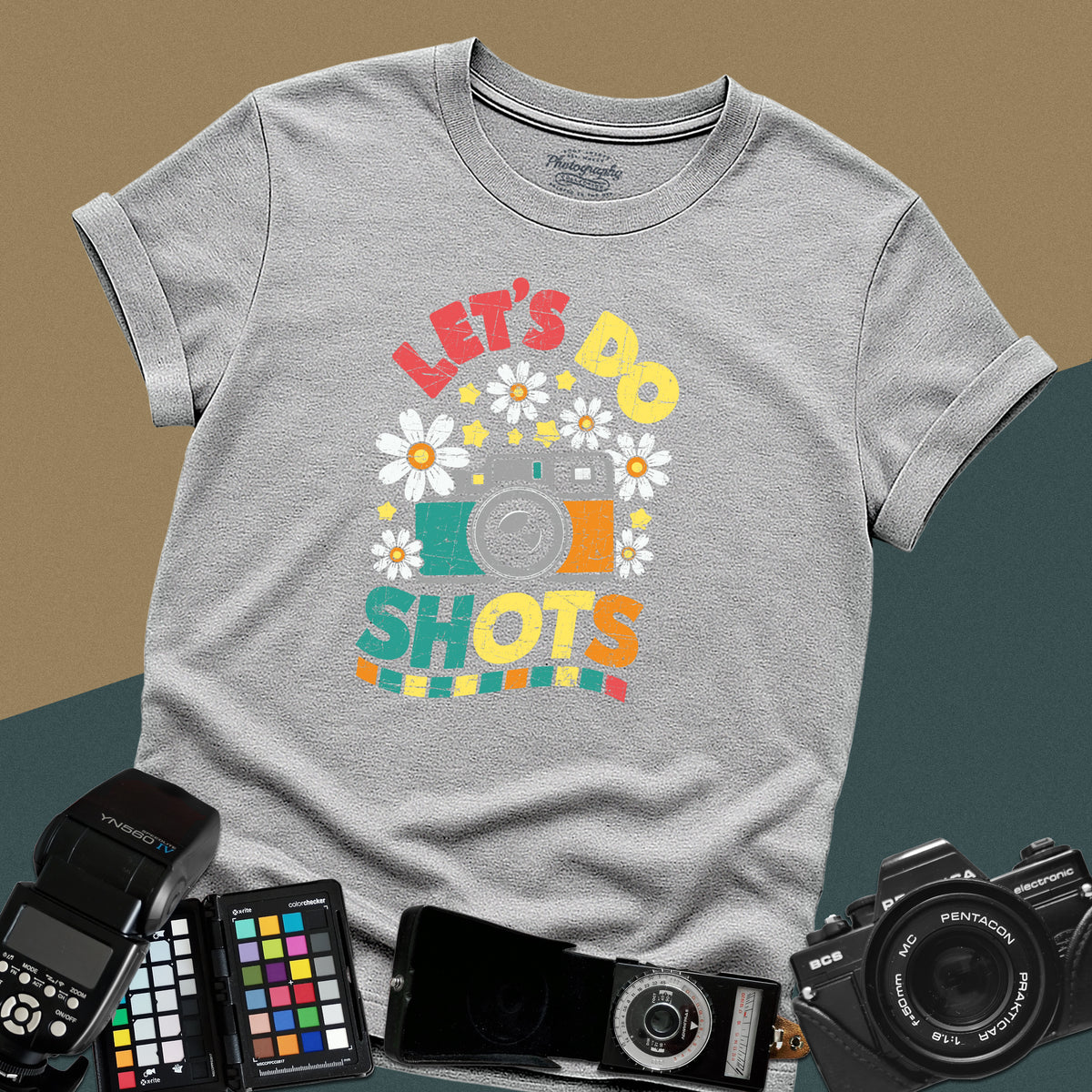 A sport grey t-shirt featuring a colorful distressed retro graphic with a camera, daisies, and stars between the text "LET'S DO" and "SHOTS" in bold block letters.
