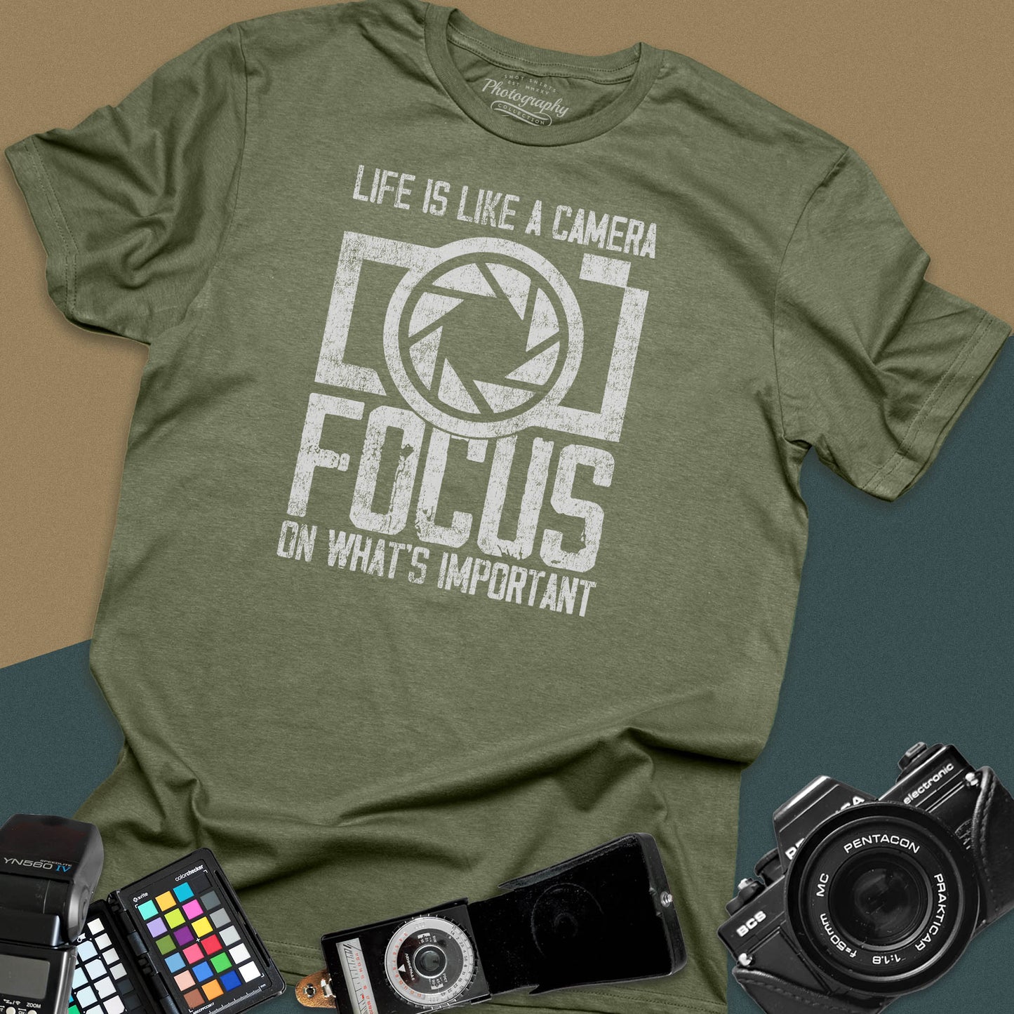 Distressed military-green t-shirt featuring a large retro camera silhouette with an aperture shutter lens graphic and inspirational photography quote typography.