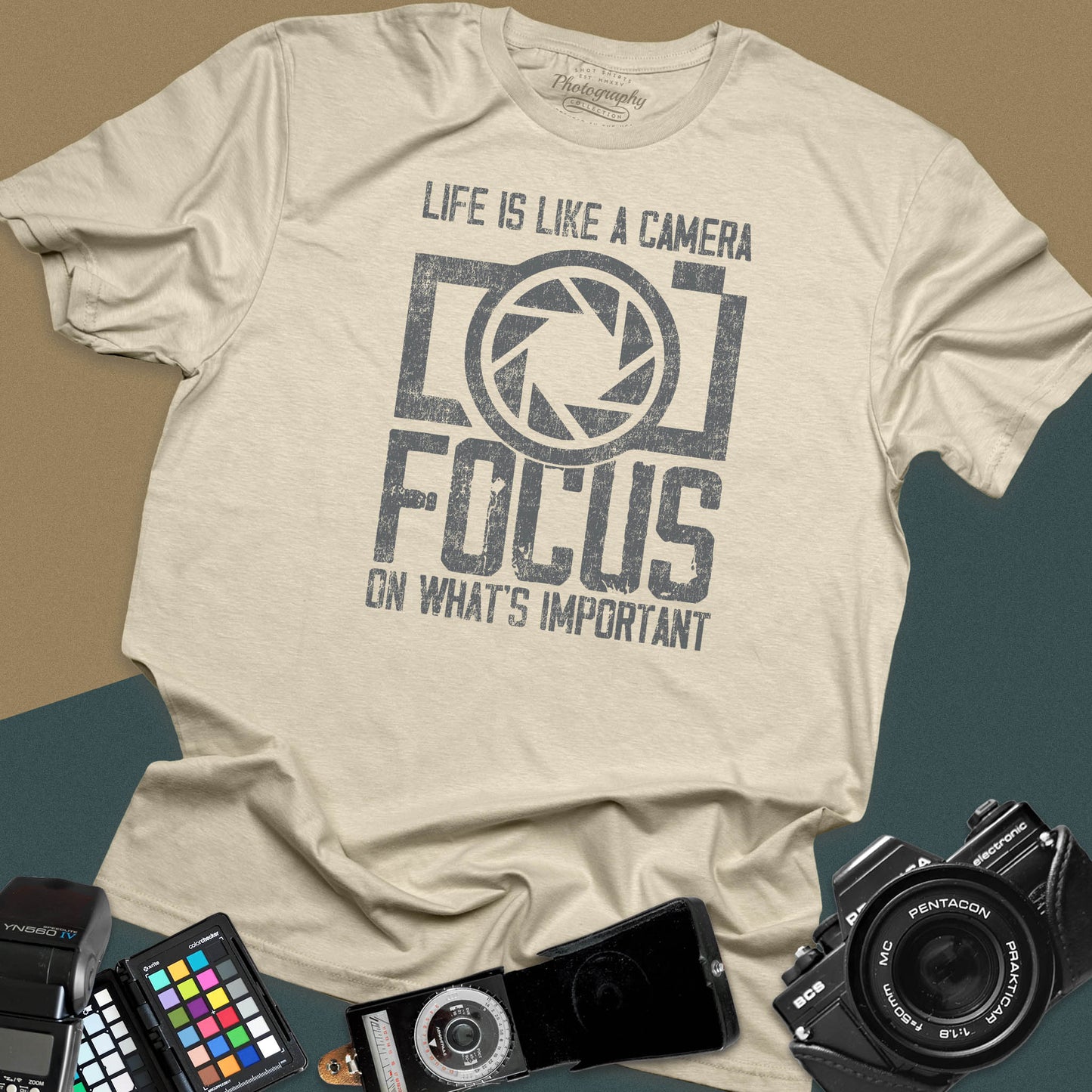 Distressed sand t-shirt featuring a large retro camera silhouette with an aperture shutter lens graphic and inspirational photography quote typography.