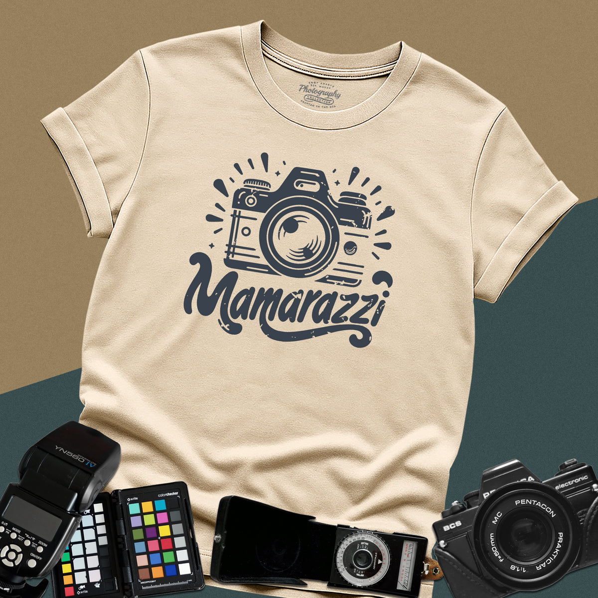 A sand t-shirt featuring a distressed vintage camera graphic with sparkles and the stylized text "Mamarazzi" written in a retro script font across the chest.