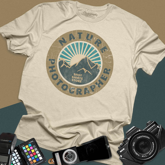 A sand t-shirt featuring a circular distressed retro graphic with mountains and a sunburst, with the words "Nature Photographer" arced around the top and bottom.