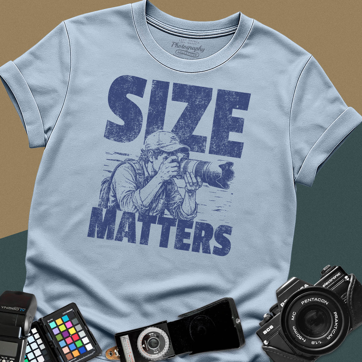 A light blue t-shirt featuring a distressed graphic of a photographer looking through a camera with a huge telephoto lens, with the words "SIZE" and "MATTERS" in bold between them.